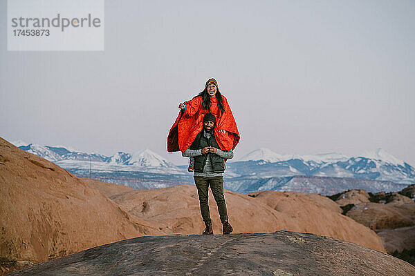 Eine Frau sitzt auf den Schultern ihrer Freundin und lacht in den Bergen