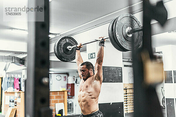 Mann mit Hanteln im Fitnessstudio macht Crossfit