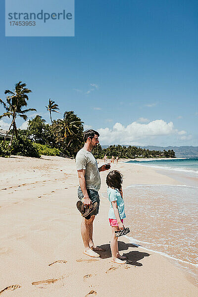 Vater und Tochter stehen am Strand von Oahu und beobachten die Wellen