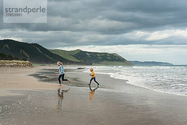 Zwei Kinder laufen an einem bewölkten Tag in Neuseeland am wunderschönen Strand