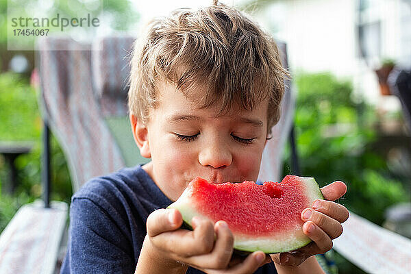 Kleiner Junge mit blonden Haaren  der mit geschlossenen Augen Wassermelone isst