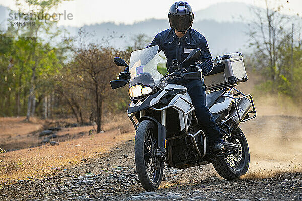 Mann fährt mit seinem Abenteuermotorrad auf einer unbefestigten Straße in Kambodscha