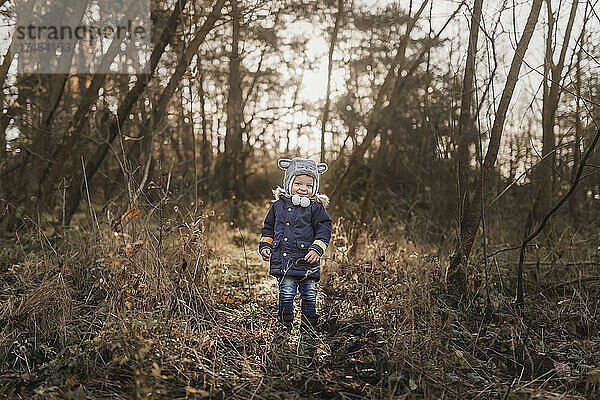 Kleiner glücklicher Junge  der im Herbst im Wald steht