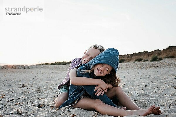 Bruder und Schwester saßen spielerisch im Sand am Strand und umarmten sich