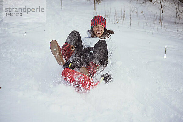 Glückliche europäische Frau lacht und rodelt den Schneehügel in der Tschechischen Republik hinunter