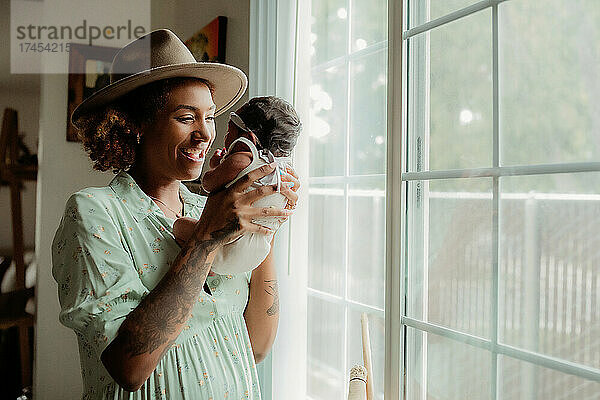 Lächelnde junge schwarze Mutter hält ihre kleine Tochter an einem Fenster