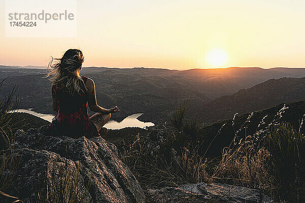 Eine Frau sitzt in der Lotus-Meditationsposition bei einem wunderschönen Sonnenuntergang.