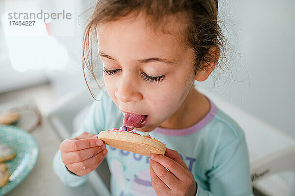 Kleines Mädchen leckt Zuckerguss vom Ostereierplätzchen
