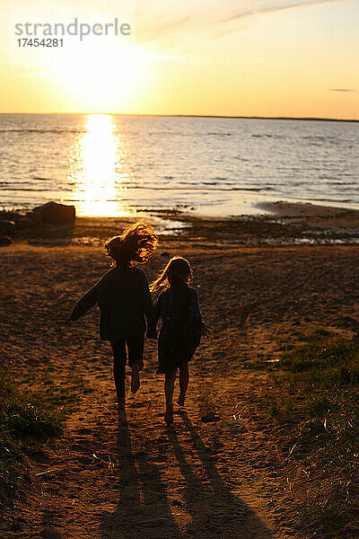 Zwei Mädchen rennen bei Sonnenuntergang zum Meer.