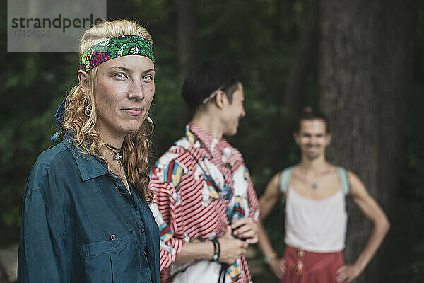 Drei farbenfrohe queere Freunde lächeln gemeinsam beim Festival im Wald