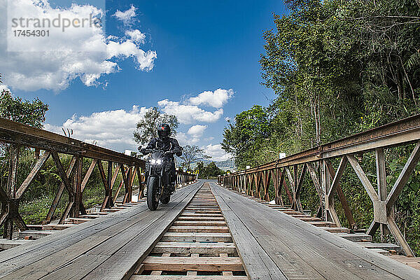 Mann fährt mit seinem Motorrad über eine Behelfsbrücke im Norden Thailands