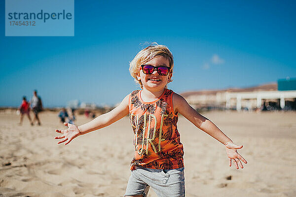 Glücklich lächelnder kleiner Junge mit Sonnenbrille am Strand