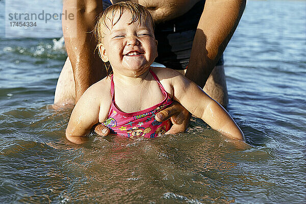 Das lächelnde Mädchen im rosa Badeanzug schwimmt und hält Papas Hände