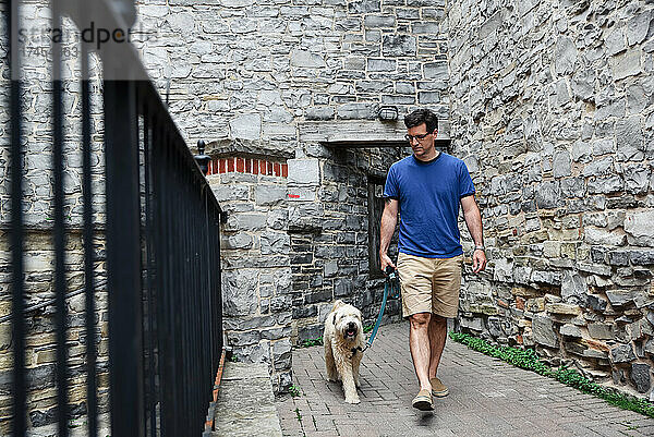 Kaukasischer Mann geht mit flauschigem Hund durch Steingasse.