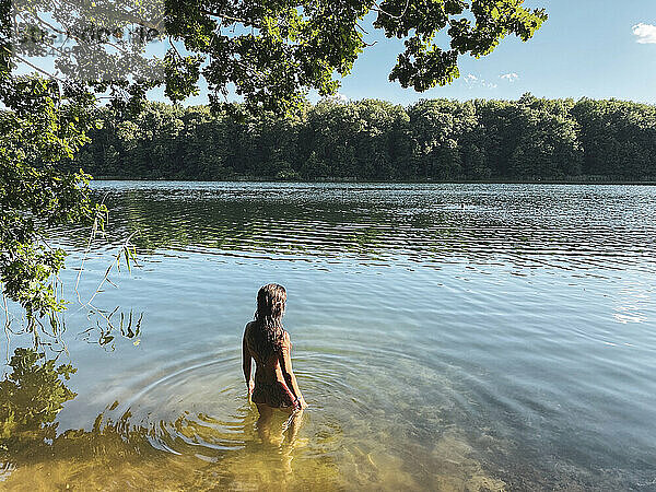 Frau steht nackt im Wald im wunderschönen grünen sandigen Seewasser