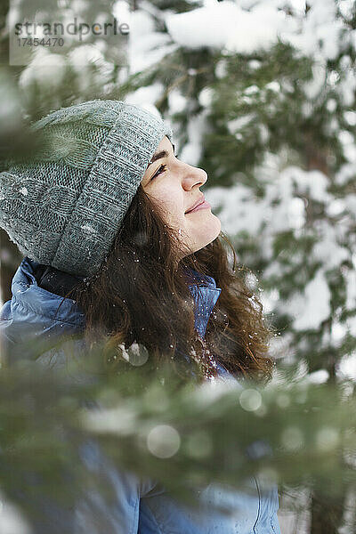 Das Porträt einer Frau  die glücklich den fallenden Schnee bewundert  schaut nach oben.