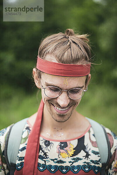 Bunter queerer Mann mit Brille lächelt in der Natur mit Schminke