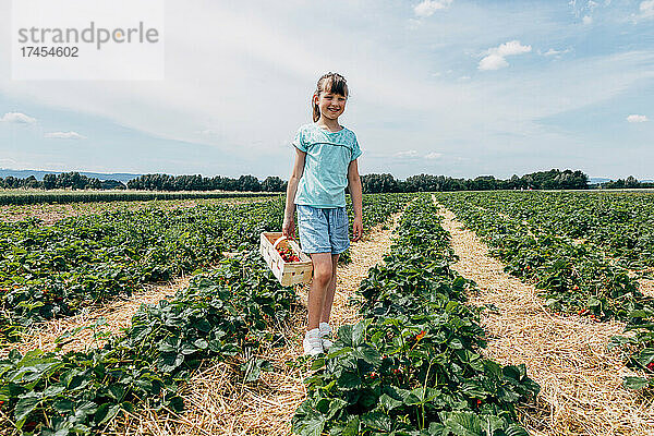 Glückliches Mädchen  mit einem Korb voller Erdbeeren in der Hand