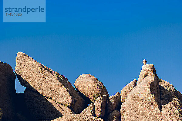 Teenager versteckt sich hinter großen Felsen in der Wüste.