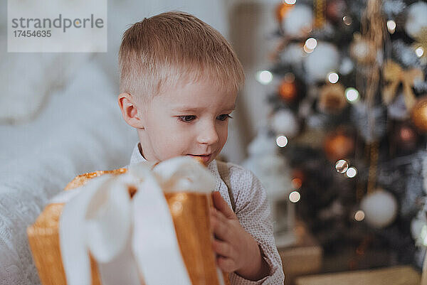 Fröhlicher  geschnittener Junge  der Geschenke unter dem Weihnachtsbaum öffnet.