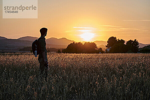 Die Silhouette eines Fotografen blickt bei Sonnenuntergang auf einer Wiese auf die Sonne