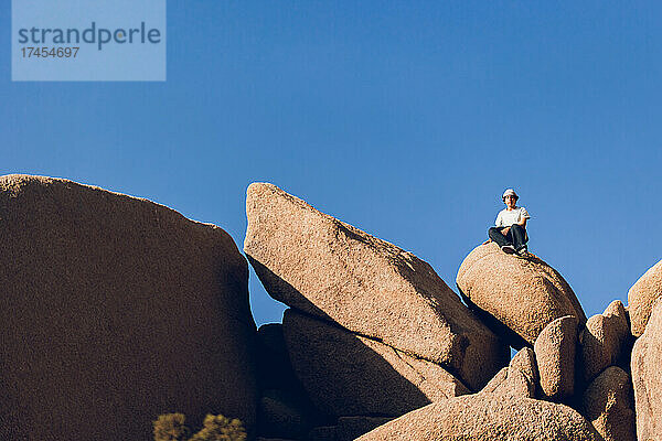Teenager sitzt an einem sonnigen Tag auf einem großen Felsen in der Wüste.