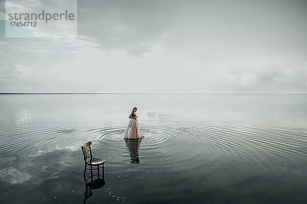 Elegante Frau stieg ins Wasser. Sonnenuntergang und Silhouette