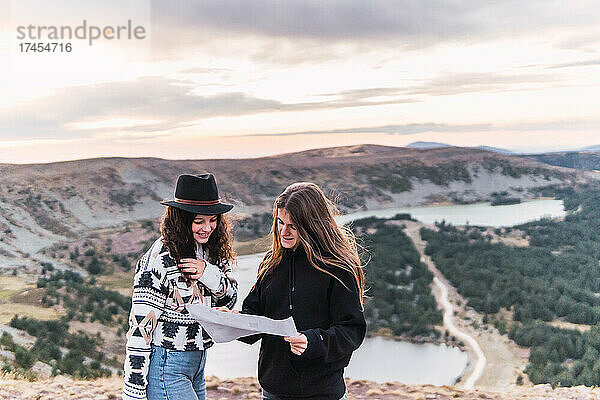 Zwei Frauen schauen auf eine Karte und stehen an einem See mit Bergen
