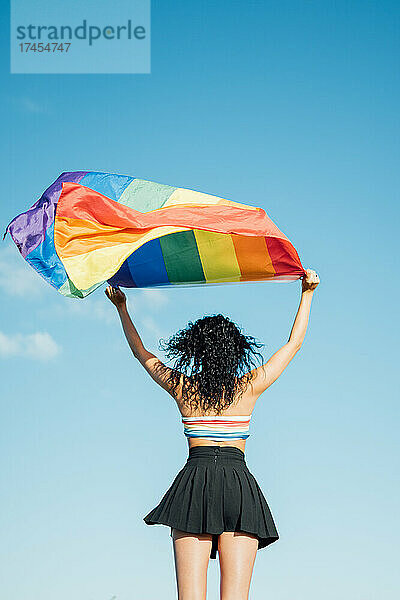 Frau auf dem Rücken mit offenen Armen  die eine LGBT-Flagge schwenkt