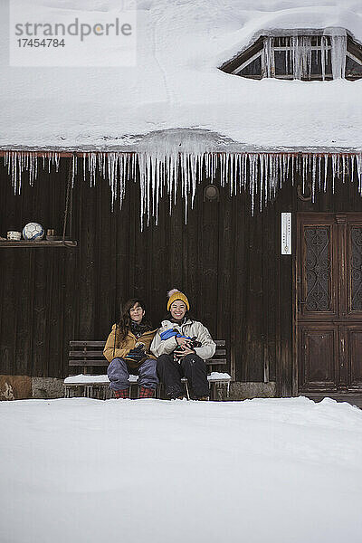 Queeres Frauenpaar lächelt und hält Hunde vor gefrorener Winterhütte