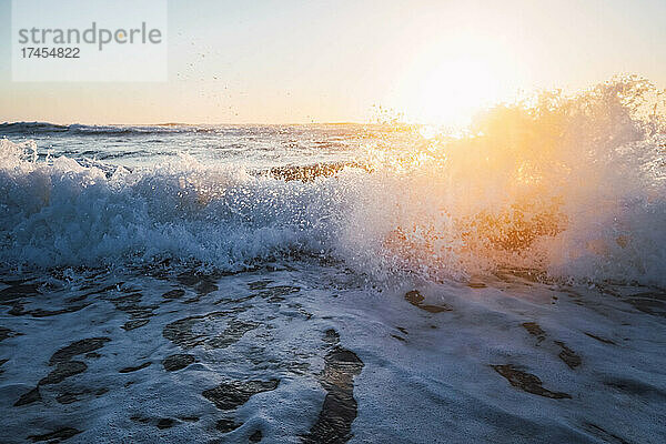 Wellen brechen am Ufer des Strandes mit Schaum bei Sonnenuntergang