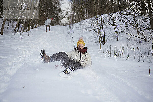 Asiatische Person lacht vor Freude  während sie auf der Rodel den Schneehügel hinunter rodelt