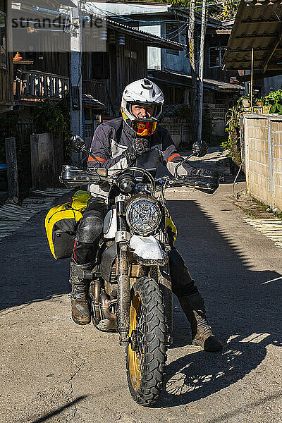 Mann hält mit seinem Motorrad in einem thailändischen Dorf auf der Straße an