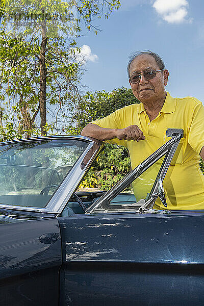 Senior adult posing proud with his restored convertible car