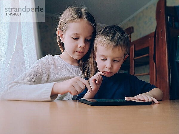 Zwei kleine Kinder mit Gadget-Tablet zu Hause am Tisch