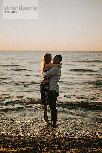 Ein Mann hält ein Mädchen in seinen Armen und umarmt sie am Meer.