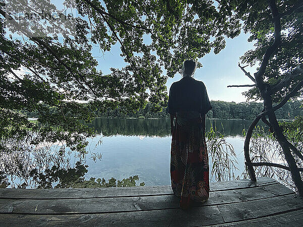 Frau im Rock blickt von der Holzplattform auf den grünen Natursee