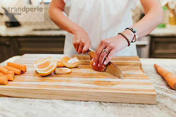 Nahaufnahme einer Frau  die in ihrer Küche Orangen auf einem Schneidebrett schneidet