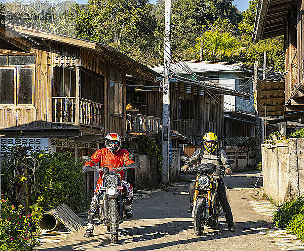 Männer halten mit ihren Motorrädern in einem thailändischen Dorf auf der Straße an