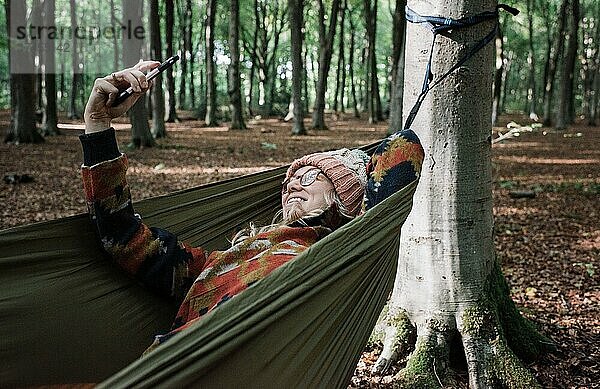 Frau liegt in einer Hängematte im Wald und macht ein Selfie