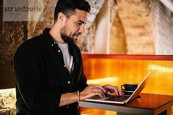 Glücklicher Geschäftsmann  der Laptop-Computer im Café benutzt