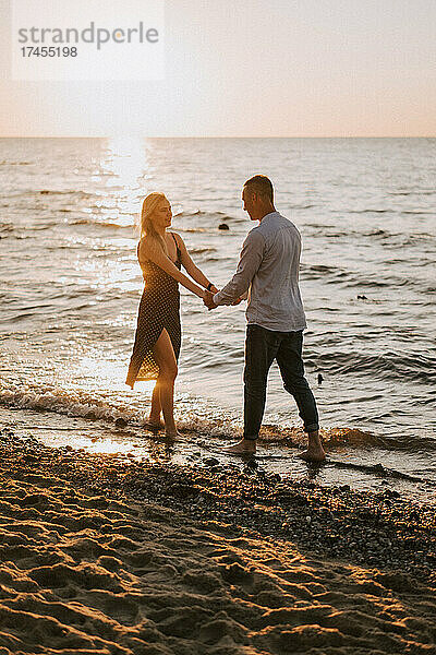 Ein junges verliebtes Paar steht Händchen haltend am Meer.