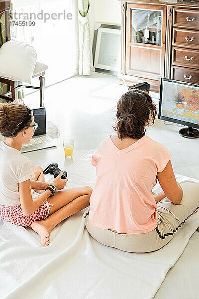 Mutter und Tochter mit Gamepads spielen zu Hause gemeinsam Videospiele