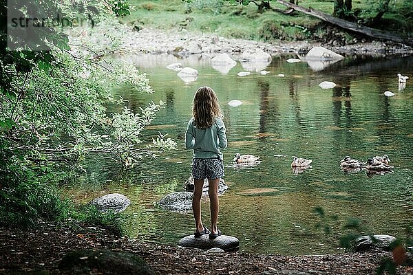 Ein junges Mädchen stand spiegelnd an einem friedlichen Fluss mit schwimmenden Enten