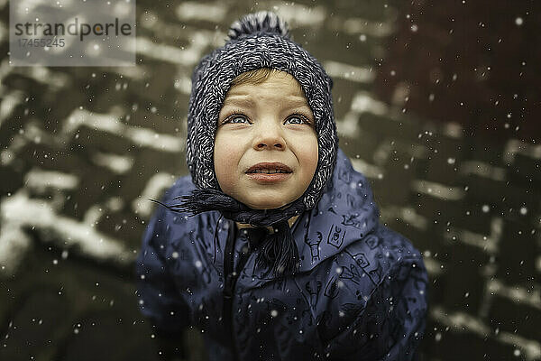 Kleiner Junge in blauer Winterkleidung  der in den schneebedeckten Himmel blickt