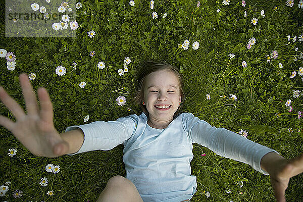 Ein fröhliches Kind liegt mit erhobenen Händen im Gras.
