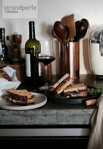 Fleisch- und Gurkensandwiches und ein Glas Rotwein auf einem Betontisch