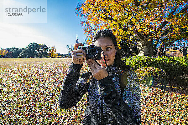Frau macht ein Foto mit einer digitalen spiegellosen Kamera in den Gärten von Tokio