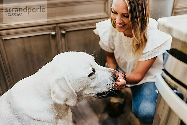 Lächelnde Frau gibt ihrem Labrador in ihrer Küche ein Leckerli