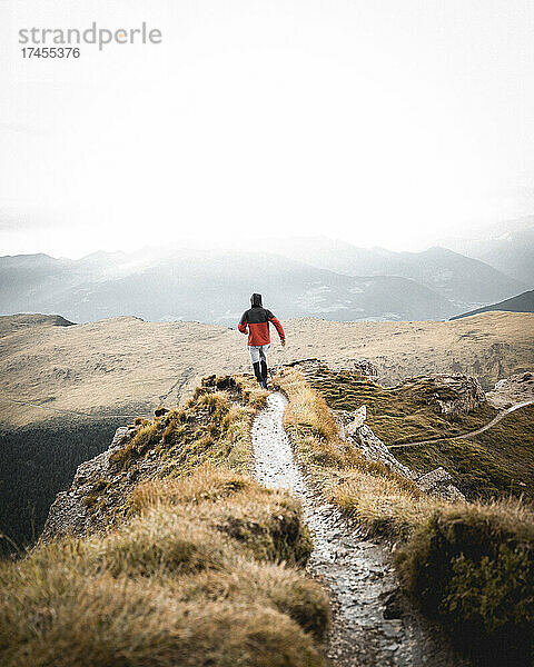 Mann in roter Jacke spaziert auf einem Bergpfad